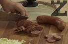 Режем наденицата на колелца, прибавяме я към ориза, отново разбъркваме.
