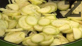 Обелваме тиквичките и ги нарязваме на тънки колелца. Поставяме ги в силно сгорещена мазнина, прибавяме и наситнения кромид лук. В началото не разбъркваме, изчакваме продуктите да се запържат за 3-4 мин.