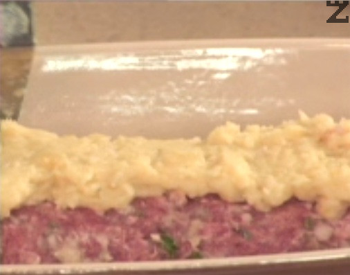Colocamos la mezcla de carne sobre papel de aluminio, le damos forma rectangular y la enrollamos. Pasamos el rollo a una fuente de horno engrasada y lo cubrimos por encima y por los lados con el puré de patatas. Alisamos la superficie con una espátula de repostería o una cuchara sopera. 
