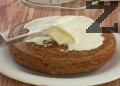 Приготвяме глазура. Разбиваме добре сирене крема, добавяме масло, пудра захар и ванилова есенция. Разбиваме около 5 мин. Нанасяме 1/3 от глазурата в средата на блата, поставяме втория блат с основата нагоре и покриваме с крема. Настъргваме лимонова кора. Оставяме тортата в хладилник за 6 часа.